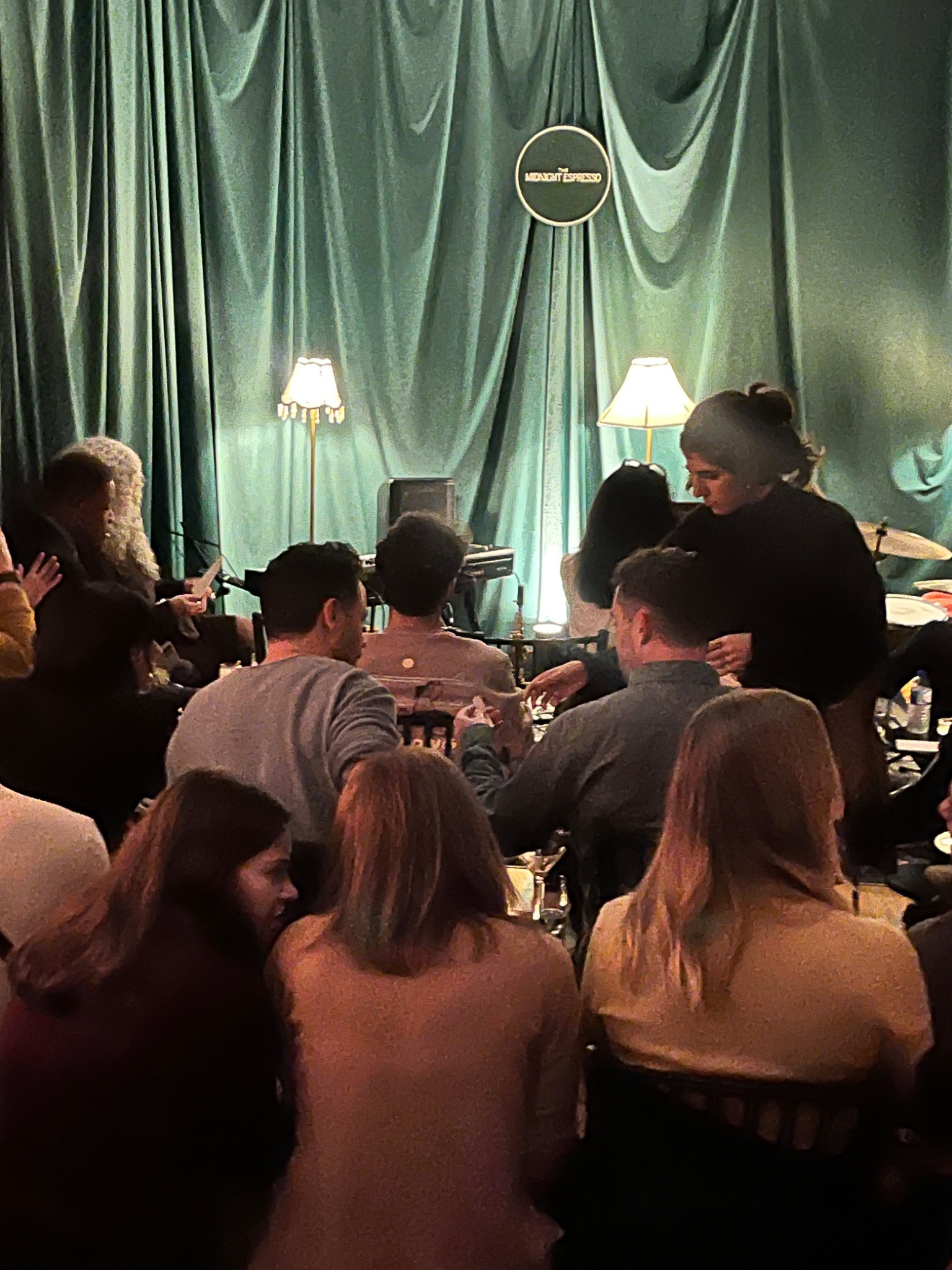 Guests seated beneath green drapery during a salon gathering.